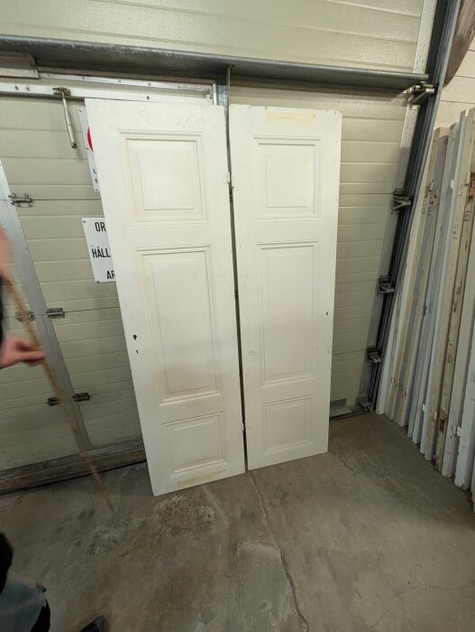Två vita, äldre stil dörrar uppställda i ett garage, med planslipade ytor och målade för att passa in i ett trähus från 1922.