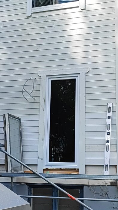 Fönster med vit foder installerad på en träfasad, byggstege och vattenpass bredvid.