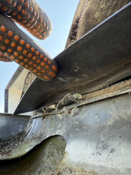 Hand i arbetshandske med verktyg försöker lossa på en metallbit som sitter fast.