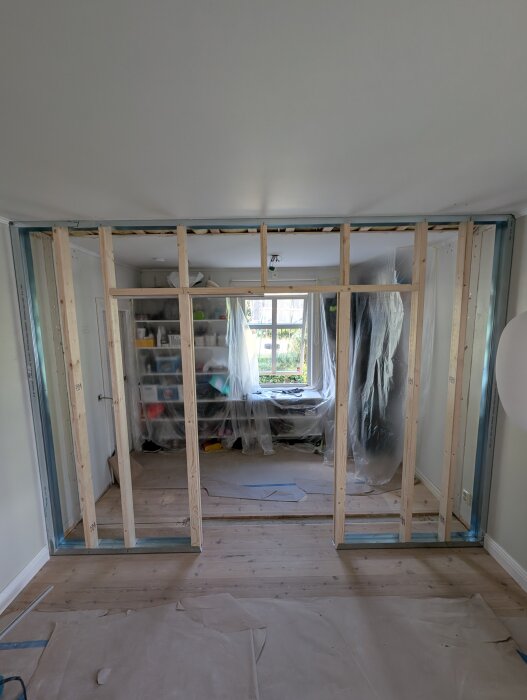 Träreglar uppsatta för ny innervägg med utrymme för skjutdörrar, material täcker golv, fönster i bakgrunden.