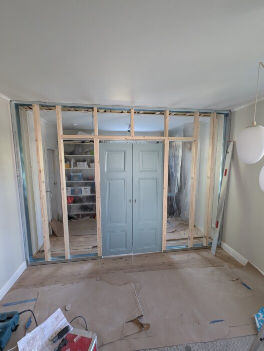 Nybyggd innervägg med skjutdörrar under installation, med reglar och sidoskenor synliga, i ett pågående renoveringsprojekt.