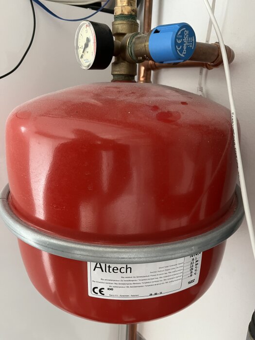Rött expansionskärl med tryckmätare och blå ventil, märkt Altech, del av ett bergvärmesystem i ett hus.