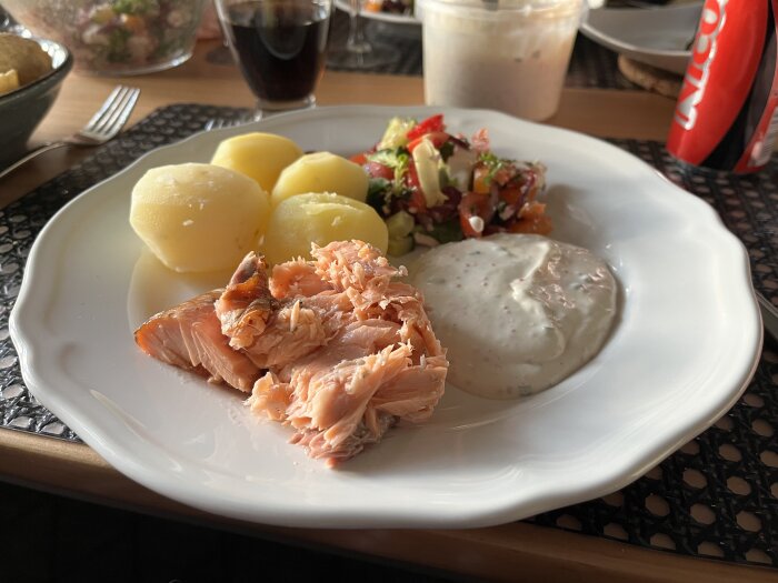Tallrik med rökt lax, kokt potatis, sallad och romsås på ett bord.