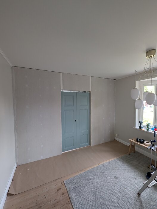 Nybyggd innervägg med dubbla skjutdörrar i blå färg, placerad mellan gipsskivor. Arbetsutrustning synlig i rummet.