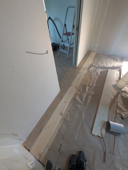 Golvarbete med nylagda träplankor där en innervägg tidigare stått, omgivna av verktyg och plast för skydd vid renovering.