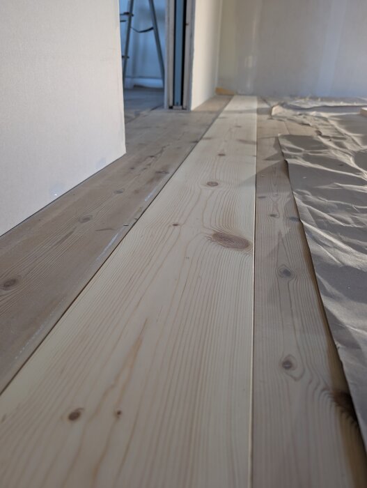 Nyslipade golvplankor lagda på ett renoverat golv där tidigare innervägg stått, med delvis ojämn yta och lite papper brett ut på sidan.