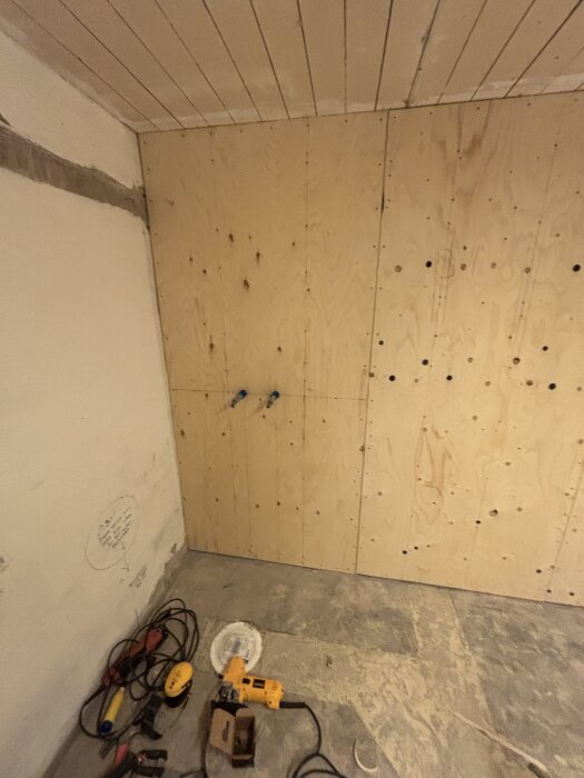 Vägg av plyfa och gips i ett rum under renovering, verktyg ligger på golvet.