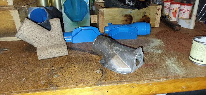 Gjuten detalj till kompressor tillsammans med blåa och bruna gjutformar och verktyg på arbetsbänk.