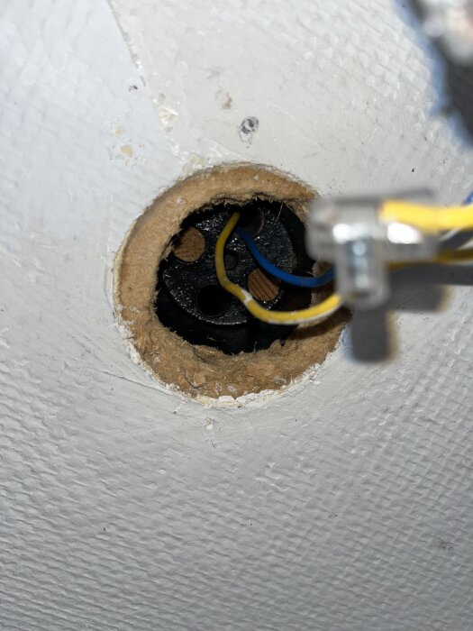 Bild på ett runt, öppet takhål med synliga elektriska kablar i blått och gult, utan fäste för DCL-uttag.