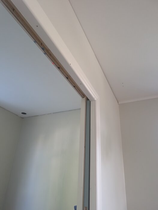 Nymålade väggar och tak med nyligen monterade dörrlister ovanför dörröppningen i ett rum under renovering.