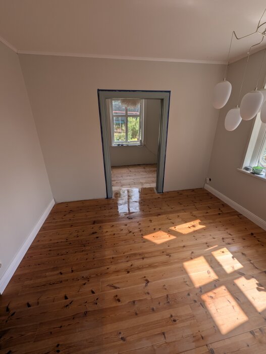 Nyrenoverat rum med såpskurade trägolv, målade väggar och monterade lister. Dörröppning med avtagbart dörrfoder syns också.