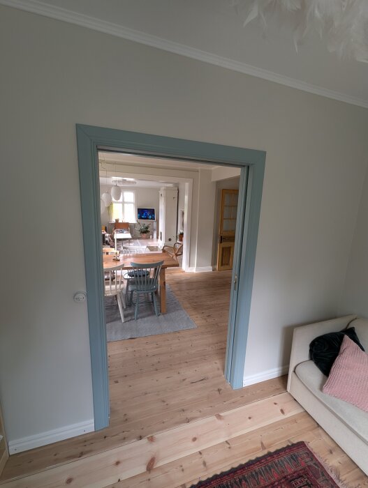 Utsikt från sovrummet genom dörröppning mot ett matsalsbord, stolar och ett rum med ljusa väggar och trägolv.