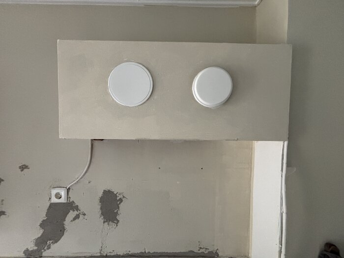 Ventilationsrör i kök täckt av en box med två runda vita täcklock, fotograferat underifrån. Insulering och väggsynliga skador.