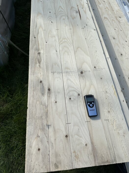 Torr bräda med mätinstrument ovanpå visar en av flera brädor, vissa torra och andra fuktiga med mögel, i ett byggprojekt.
