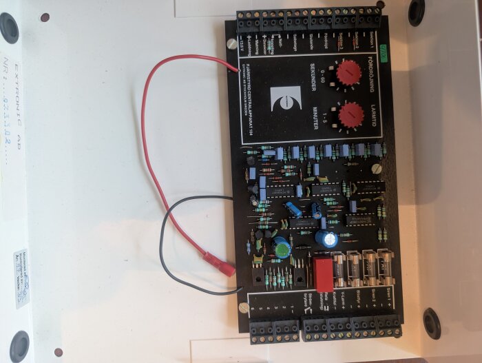 Oanvänt larm från slutet av 90-talet med kretskort och kopplingsscheman, liggande på en vit yta med röda och svarta kablar.