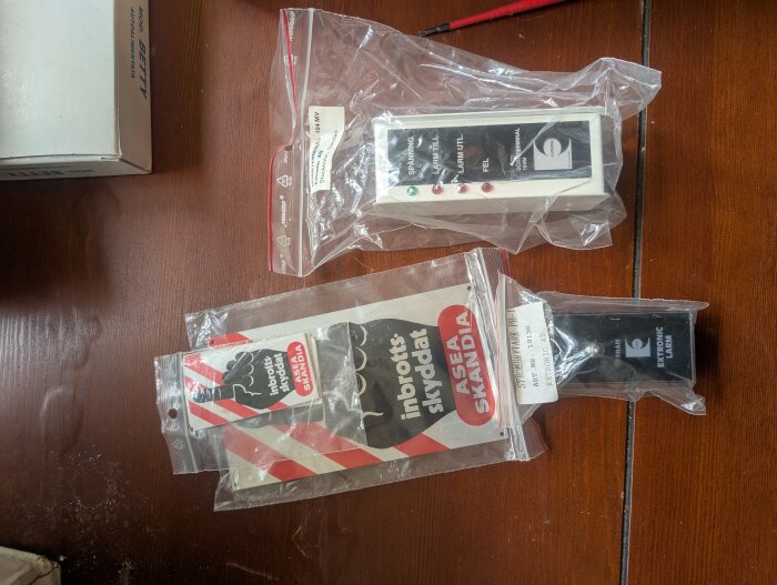 Gamla larmsystemdelar från slutet av 90-talet i originalförpackningar på ett bord, inklusive ett kontrollpanel och sensorer.