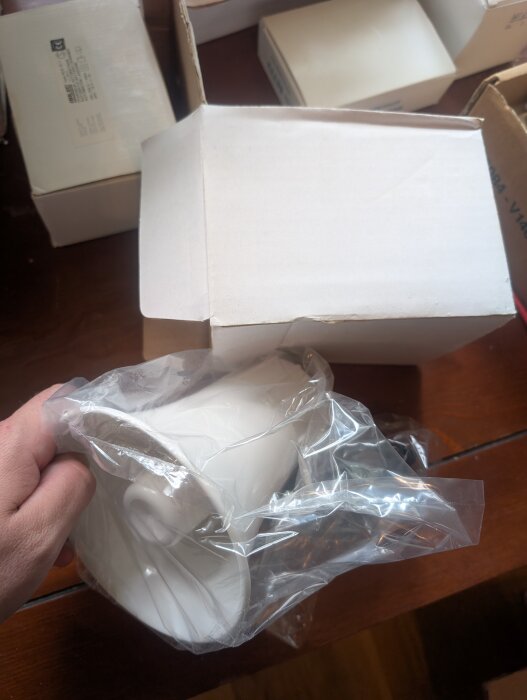 Oanvänt 90-talslarm med vit komponent i plastpåse, på ett bord med kartonger i bakgrunden.