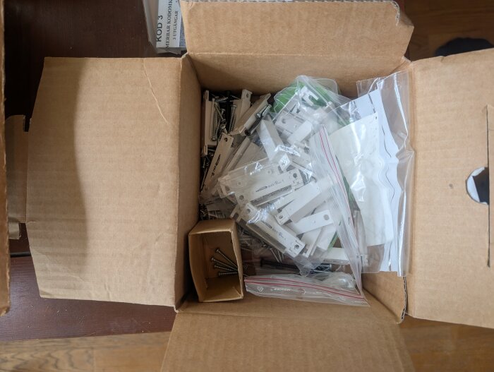 Kartong med komponenter till ett äldre larm, inklusive små påsar och skruvar.