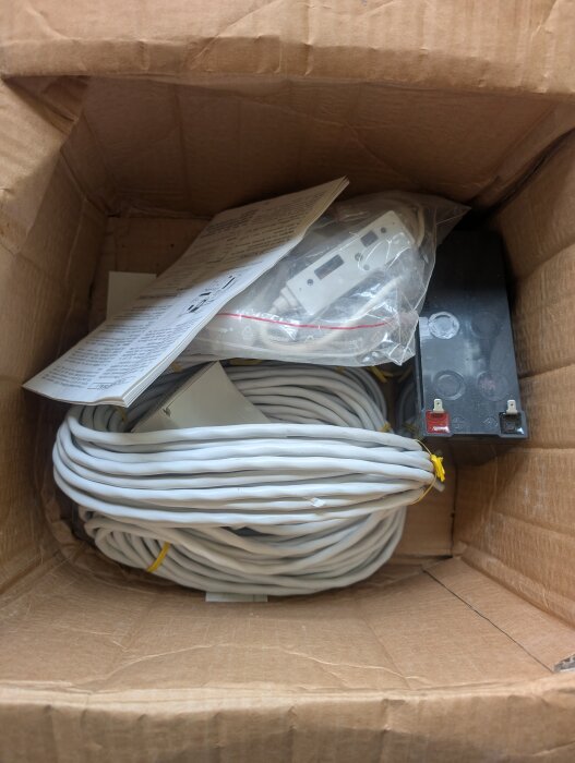 Oanvänt 90-tals larm med kablar, komponenter och dokumentation i en kartong.