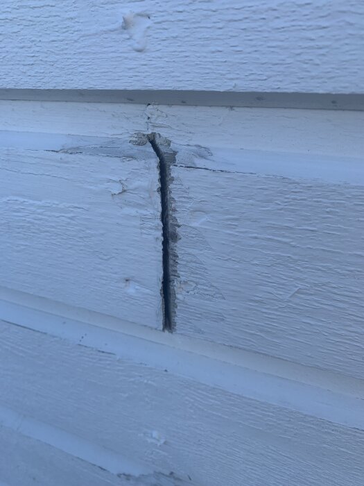 Glipa i vit träfasad som behöver lagas innan målning.