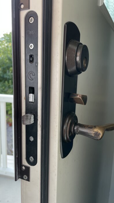Inzoomad bild på en dörr med öppet dörrhandtag och synligt låshus av märket Assa samt en brunoxiderad dörrknopp.