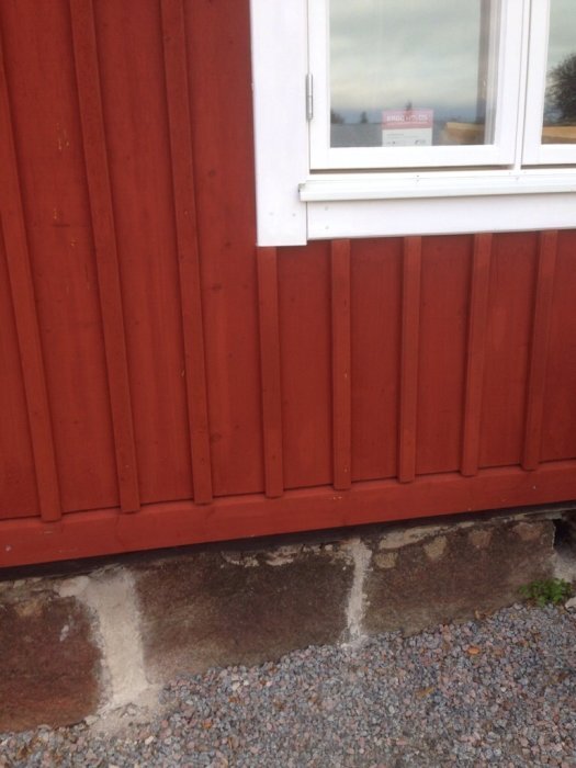 Röd husfasad med vit fönsterkarm. Rubrik på fönstret, stenfundament synligt nedtill.