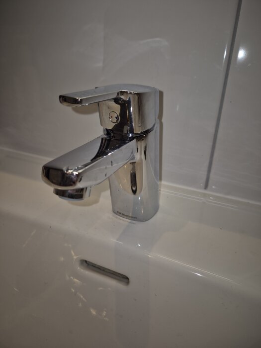 Kromad tvättställsblandare i ett badrum, monterad på en vit porslinsho, tidigare utbytt på grund av sprucken insats.