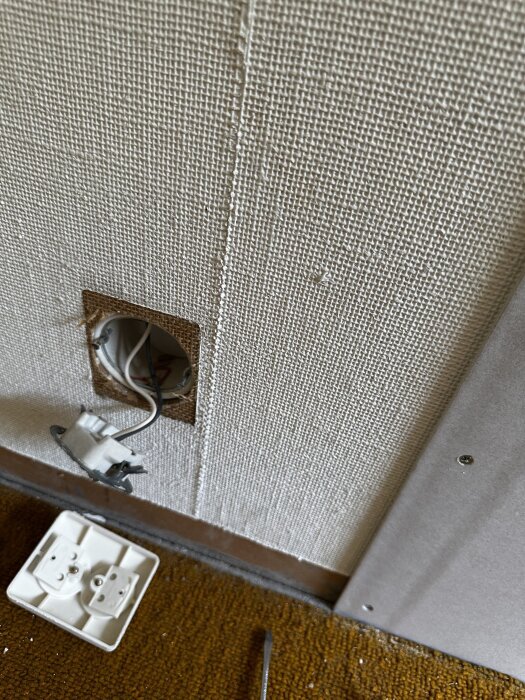 Vägg med renoveringsgips och ett öppet eluttag med synliga kablar; uttagslocket ligger på golvet bredvid.