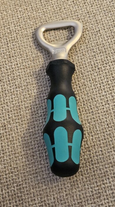 Flasköppnare från Wera med ergonomiskt handtag i svart och turkost liggandes på en beige yta.