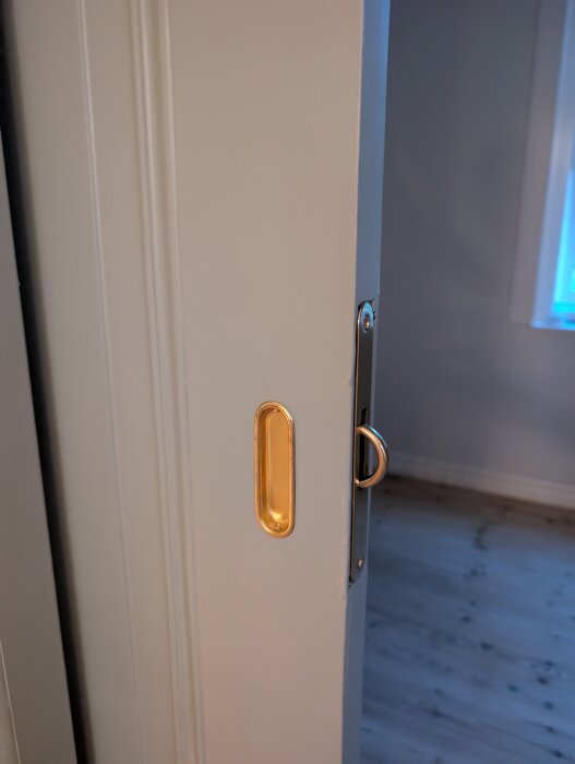Närbild på en dörrkant med fastsatt metallskena och gyllene beslag för skjutdörr.