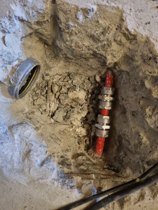 Lagning av röd slang med koppling i vägg, omgiven av murbruk och byggdamm i väntan på elvärmegolv.