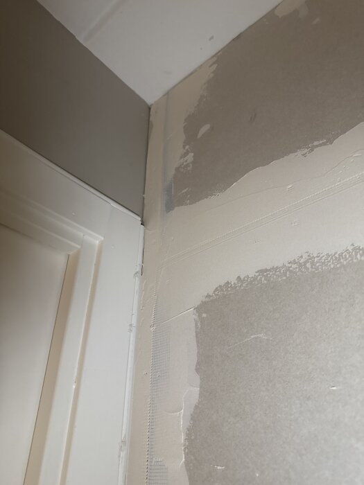 Närbild av en gipsvägg i ett hörn, delvis spacklad med synliga skarvaremsor. Dörrkarmens närhet gör hörnet svår att arbeta med.