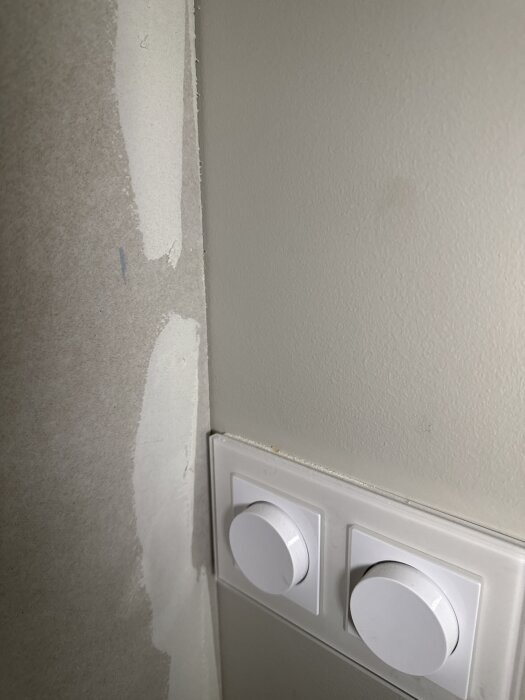 Vägg med spackelarbete nära en dubbelströmbrytare i ett vardagsrum under renovering.