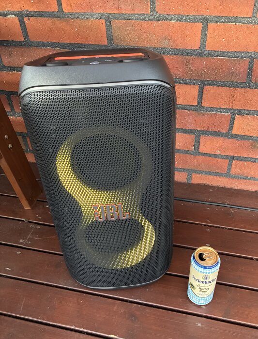 BT-högtalare av märket JBL och en burk öl på en träyta framför en tegelvägg.