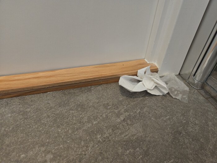 Pappersservetter vid en tröskel, delvis våta, i ett badrum med ljusa väggar och en dörrkarm mot golv i stenliknande material.