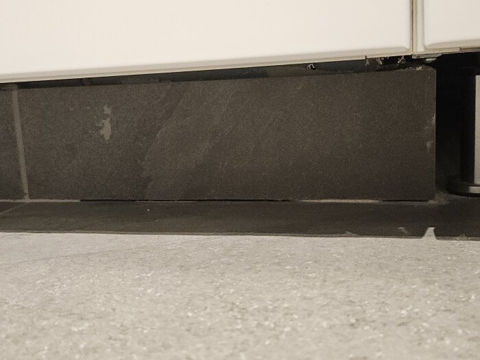 Svart klinkerplatta under vit skåplucka, eventuellt problem med tätning och silikon saknas vid duschvägg och blandare, oro för vattenskada.