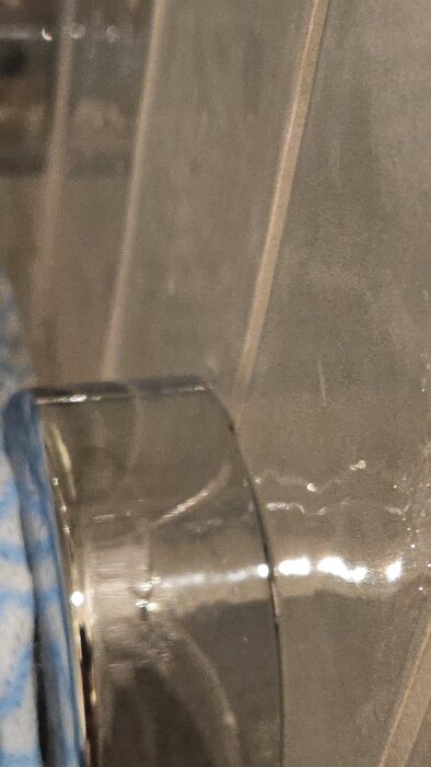 Närbild på en duschhandtag, där vattendroppar syns på ett kaklat badrumsvägg med fokus på foglinjer och potentiell brist på silikon.