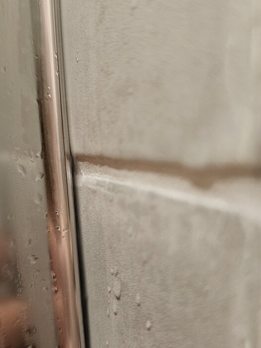 Närbild av en duschväggslist där vatten rinner, visar avsaknad av silikon och potentiell risk för läckage vid duschens kant.