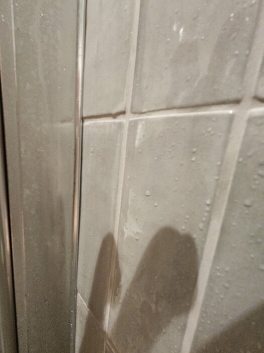 Vägg i dusch med kakel plattor, synliga vattenfläckar och skarvar utan silikon, potentiell fuktproblematik under renovering.