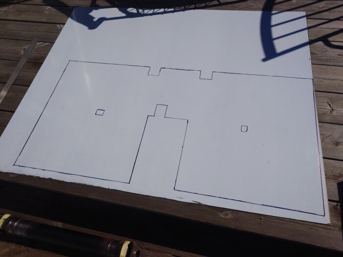 En stor aluplåt med markerade utskärningar ligger på ett trädäck, redo att formas.