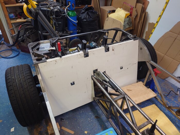 Byggprojekt med ram gjort av aluplåt, däck och svetsad tank i verkstadsmiljö. Verktyg och material synliga i bakgrunden.