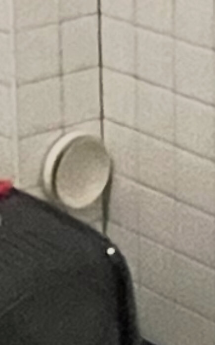 Ventil på vägg i rum med vita, kvadratiska kakelplattor.