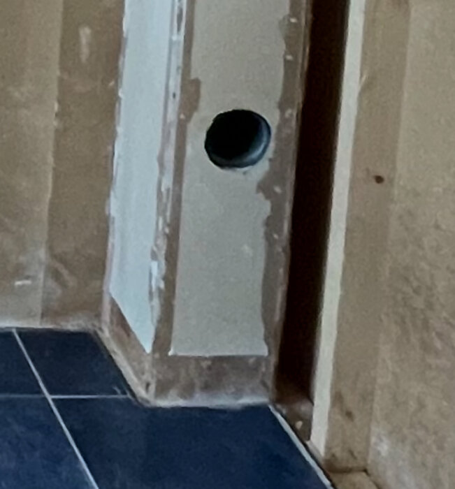 Gipsad vägg med hål för ventilation i ombyggt rum från bastu/badrum till sovrum, bredvid blått klinkergolv.