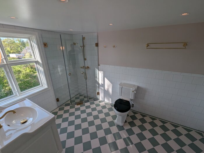 Nytt renoverat badrum med schackrutigt golv, vitkaklade väggar, duschkabin, wc, handfat och fönster med utsikt över grönska.