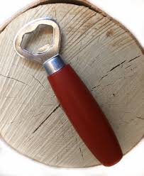 En kapsylöppnare med rött handtag placerad på en träskiva.