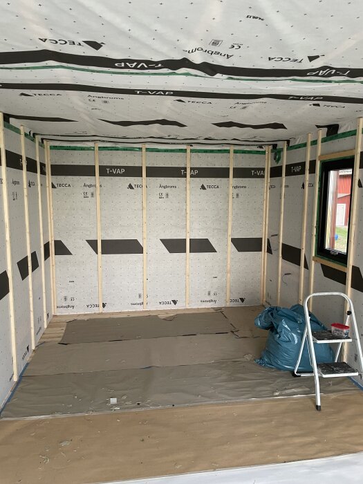 Basturum under renovering med nyligen installerad ångbroms och träreglar, stege och verktyg. Förberett för att sätta slätspontpanel.