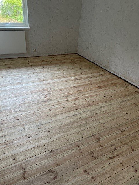 Trägolv i ett rum med ljusa väggar, tidigare täckt av en plastmatta, visar jämnhet för framtida laminatläggning.
