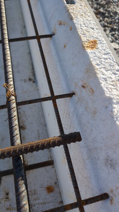 Armeringsjärn som vilar på skumplast kan ses i närbild. Järnet har rostfläckar och träder in i skumplasten med cirka en centimeter.