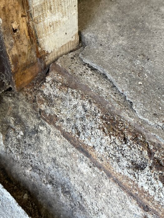 Sprucken och rostig garageinfart med skadad cement och synliga trädelar.