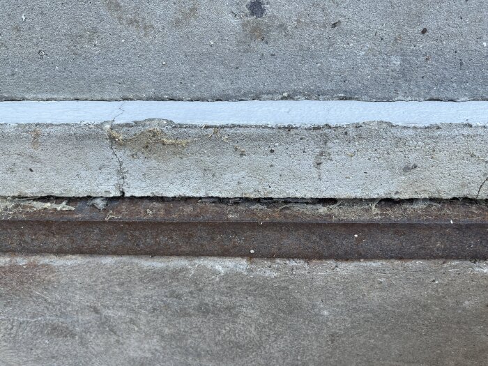 Sprucken cement i garageinfart med rostig L-profil.